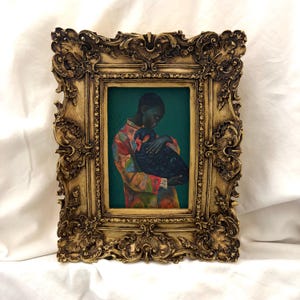 May include: A rectangular painting in an ornate, antique-style gold frame. The artwork depicts a person with short hair wearing a colorful, patterned shirt, holding a large black bird against a solid, deep teal background.