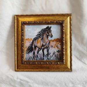 May include: Oil painting in a gold frame depicting a horse in a field. The horse is brown and black with a flowing mane. The background shows tall grass and a light blue sky. The frame has an ornate design.
