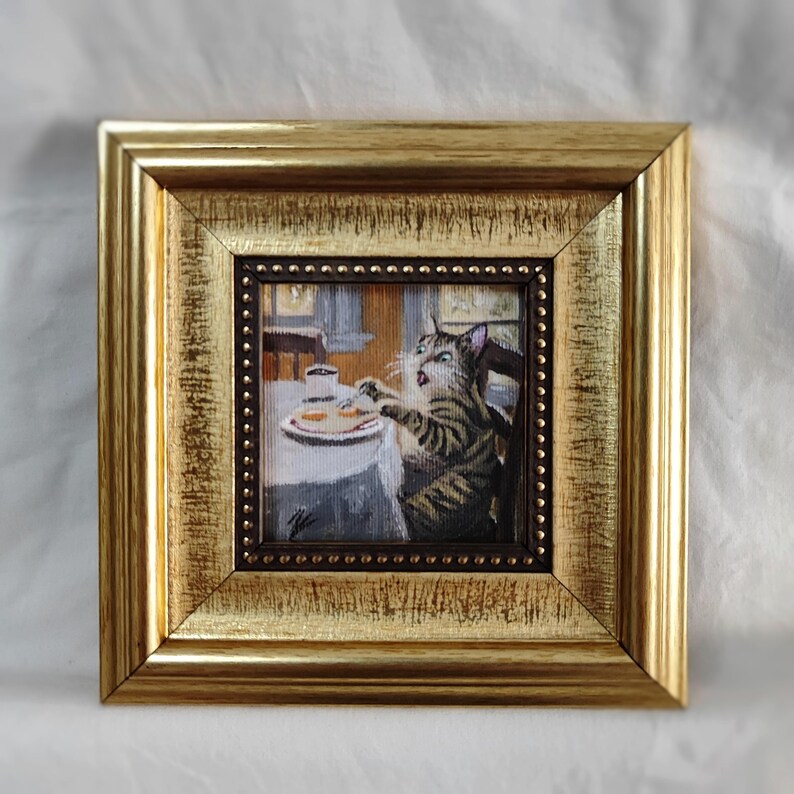 May include: A framed painting of a cat sitting at a table with a plate of food and a cup of coffee. The cat is looking at the food with a surprised expression.