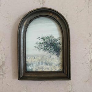 May include: An arched, framed painting of a tree in a field. The tree has green and white foliage. The field is a mix of white and yellow. The frame is dark brown with a distressed finish. The sky is a pale blue.