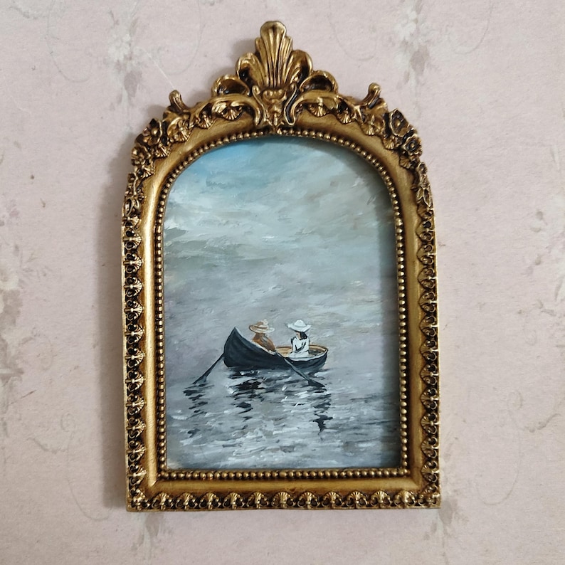 Puede incluir: Una pintura enmarcada de dos personas en un bote en un lago. La pintura est&aacute; en un marco dorado con un dise&ntilde;o decorativo.