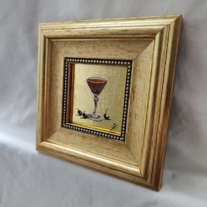 Peut inclure: Peinture encadr&eacute;e d'un cocktail dans un verre &agrave; martini avec des olives. L'&oelig;uvre est plac&eacute;e sur un fond dor&eacute; et encadr&eacute;e dans un cadre en bois dor&eacute;. La peinture est de format carr&eacute;.