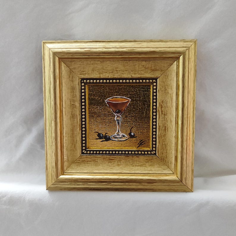 Peut inclure: Peinture encadr&eacute;e d'un cocktail dans un verre &agrave; pied, garni de cerises. L'&oelig;uvre est pos&eacute;e sur un fond dor&eacute; et encadr&eacute;e dans un cadre en bois dor&eacute;. La peinture est carr&eacute;e et repr&eacute;sente un cocktail brun.