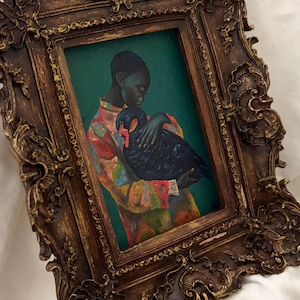 May include: An oil painting in a dark, ornate, gold-toned frame featuring a person with dark skin wearing a colorful, patterned shirt while holding a black swan against a deep green background. The frame has intricate, raised, carved-style details.