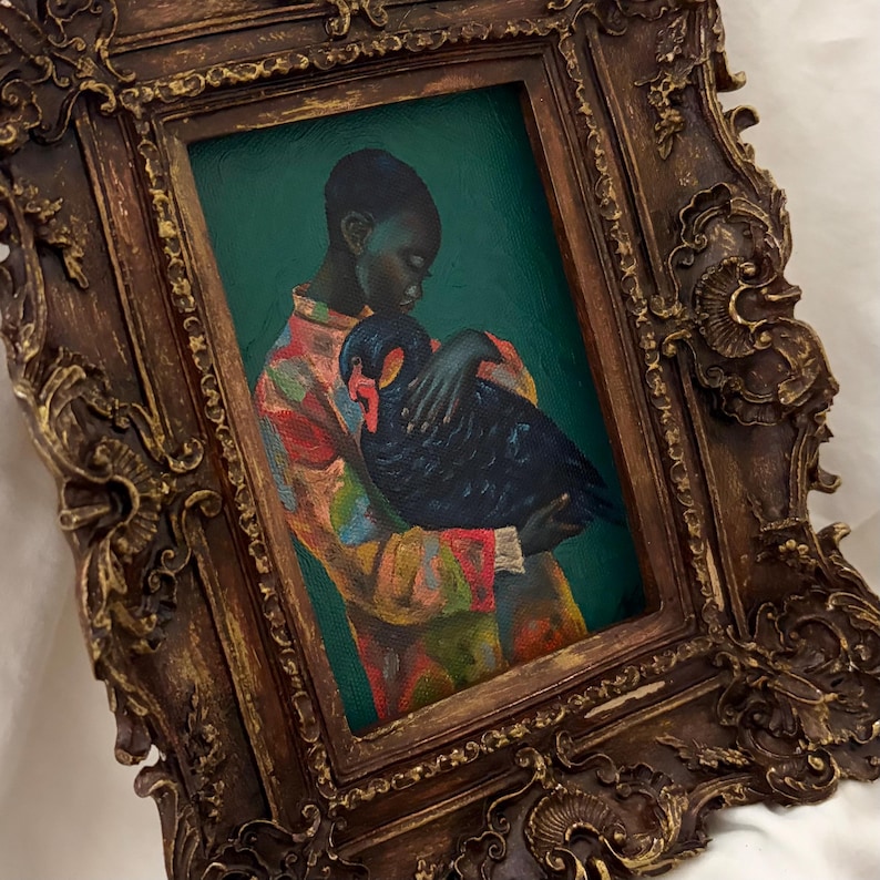 May include: An oil painting in a dark, ornate, gold-toned frame featuring a person with dark skin wearing a colorful, patterned shirt while holding a black swan against a deep green background. The frame has intricate, raised, carved-style details.