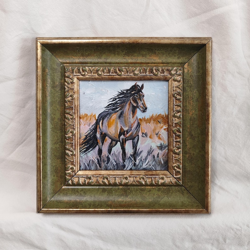 May include: A framed painting of a brown and black horse in a field of tall grass. The horse has a flowing mane and tail. The frame is a dark green with gold accents.