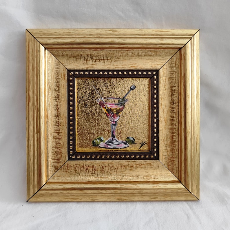 May include: A framed painting of a martini glass with olives, painted in a realistic style with a gold background.