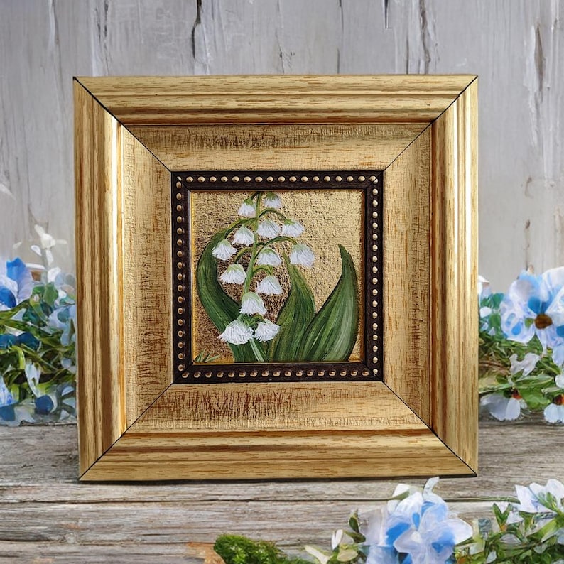 Peut inclure: Peinture encadr&eacute;e de fleurs de muguet. L'&oelig;uvre pr&eacute;sente des fleurs blanches en forme de cloche et des feuilles vertes sur un fond dor&eacute;. Le cadre dor&eacute; a une finition textur&eacute;e, ajoutant de l'&eacute;l&eacute;gance &agrave; l'art floral. Dimensions : environ 15 cm x 15 cm.