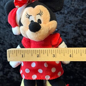 May include: A Minnie Mouse plush doll wearing a red dress with white polka dots, a matching bow, and yellow shoes with red bows. The doll has black ears and a black nose. The doll is approximately 4 inches tall.