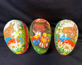 May include: Three decorative Easter eggs with colorful illustrations. One egg features a brown hen with yellow chicks and painted Easter eggs. The other two eggs have a brown bunny with a pink bow. Each egg has a red stripe.