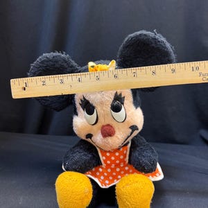 Puede incluir: Un peluche vintage de Minnie Mouse con orejas negras, un vestido de lunares rojos y blancos y pies amarillos. El juguete mide aproximadamente 15 cm de altura.