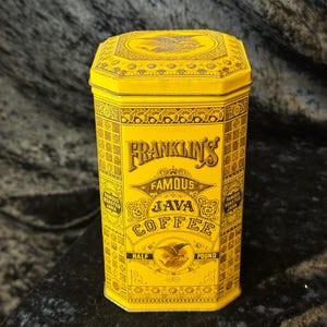 Puede incluir: Una lata amarilla vintage de café Java Famous de Franklin. La lata tiene forma octogonal con detalles ornamentados y las palabras "Franklin's Famous Java Coffee" en una fuente decorativa. La lata está etiquetada como "Half Pound" y "Famous Roasted Java".