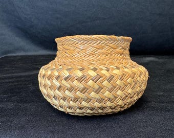 Könnte beinhalten: Ein kleiner, runder geflochtener Korb mit ausgestelltem Rand. Der Korb besteht aus naturbelassenen Schilfrohren und hat ein strukturiertes, gemustertes Design. Der Korb ist wahrscheinlich handgefertigt und eignet sich zur Aufbewahrung oder Dekoration.