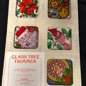 May include: A set of five vintage glass Christmas tree ornaments. Each square ornament features a different design, including a poinsettia, a lion with a lamb, Santa Claus, a cardinal, and a candle. The set is labeled "Glass Tree Trimmer."