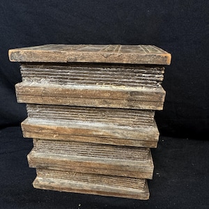 Puede incluir: Una pila de bloques de madera, que se asemeja a una pila de libros. Los bloques son de color marr&oacute;n c&aacute;lido con vetas y textura de madera visibles. Los bordes est&aacute;n ligeramente desgastados, lo que les da un aspecto r&uacute;stico. Los bloques est&aacute;n apilados ordenadamente, creando una forma rectangular s&oacute;lida.