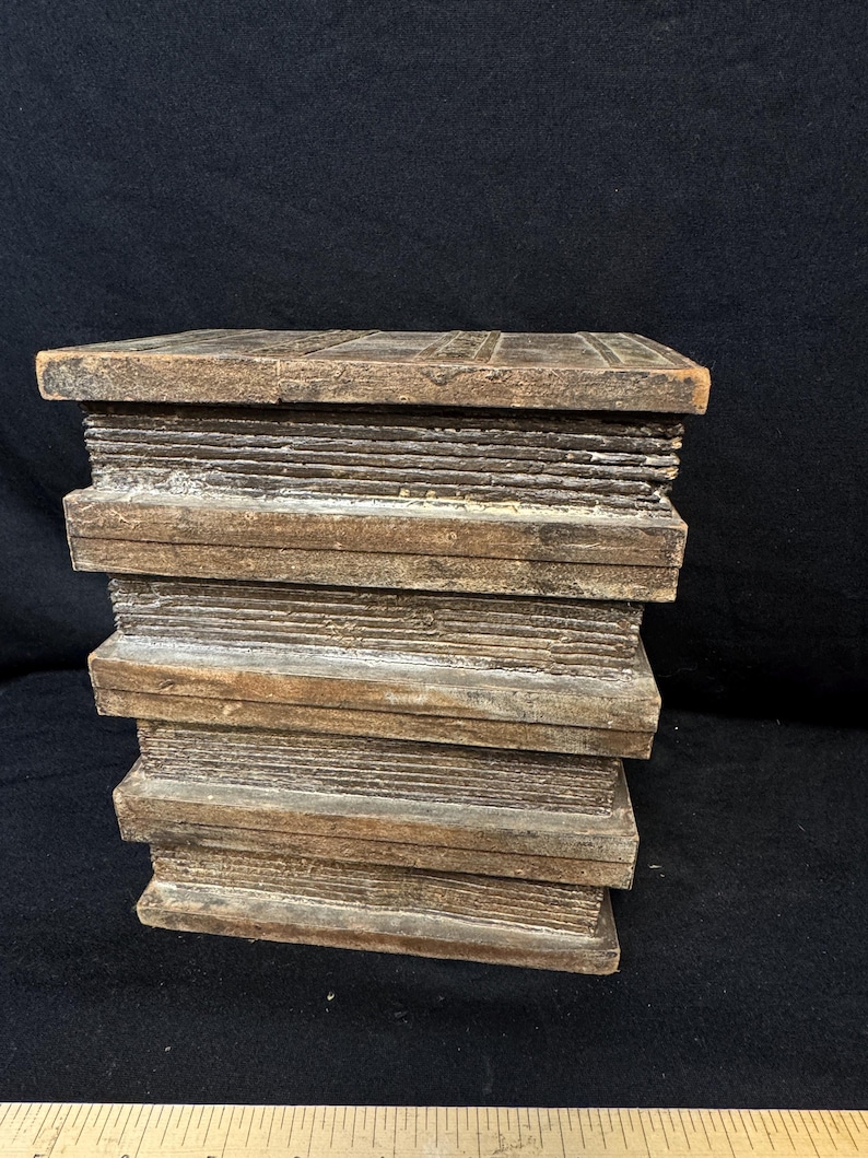 Puede incluir: Una pila de bloques de madera, que se asemeja a una pila de libros. Los bloques son de color marr&oacute;n c&aacute;lido con vetas y textura de madera visibles. Los bordes est&aacute;n ligeramente desgastados, lo que les da un aspecto r&uacute;stico. Los bloques est&aacute;n apilados ordenadamente, creando una forma rectangular s&oacute;lida.