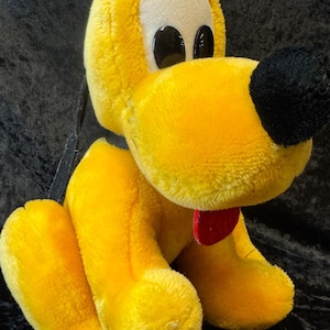 May include: A plush yellow dog toy with a black nose, large black eyes, and a red collar. The dog has large floppy ears and is sitting down. The toy is made of a soft, fuzzy material.