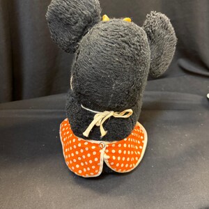 Puede incluir: Un peluche vintage de Minnie Mouse, visto desde atr&aacute;s. El peluche tiene pelo negro, orejas grandes y redondas y un cuello de vestido de lunares rojos y blancos. Un peque&ntilde;o lazo amarillo est&aacute; en la parte superior de la cabeza.