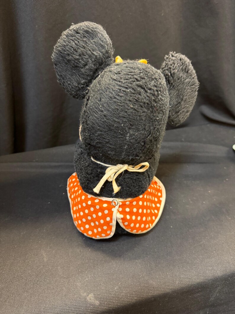 Puede incluir: Un peluche vintage de Minnie Mouse, visto desde atr&aacute;s. El peluche tiene pelo negro, orejas grandes y redondas y un cuello de vestido de lunares rojos y blancos. Un peque&ntilde;o lazo amarillo est&aacute; en la parte superior de la cabeza.