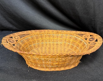 Puede incluir: Una cesta tejida de forma ovalada con un cuenco ancho y poco profundo. La cesta está hecha de fibras de color natural, con un borde decorativo con patrones circulares. Sus dimensiones son de aproximadamente 30 cm de largo, 20 cm de ancho y 8 cm de profundidad.