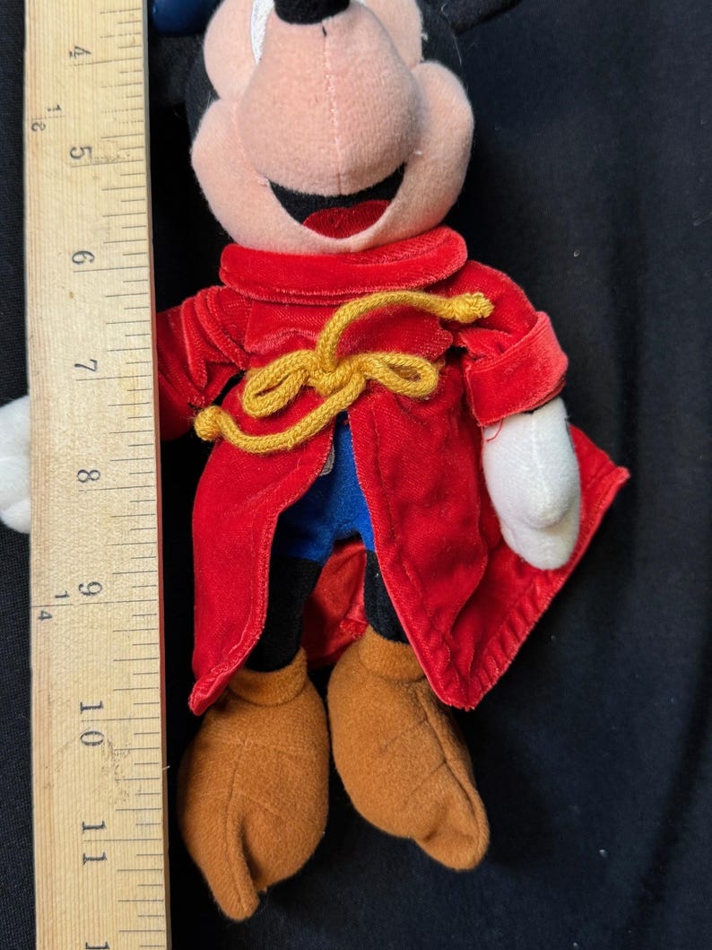 K&ouml;nnte beinhalten: Eine Pl&uuml;schpuppe von Mickey Mouse mit einem roten Samtmantel und einer goldfarbenen Krawatte. Die Puppe hat braune Schuhe, eine schwarze Hose und wei&szlig;e Handschuhe. Die Puppe ist etwa 28 cm gro&szlig;.