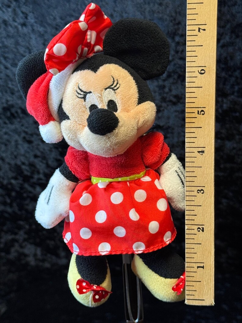 May include: A Minnie Mouse plush doll, featuring a red dress with white polka dots, a matching bow, and yellow shoes. The doll has black ears and a red and white polka dot bow. The doll measures approximately 6 inches in height.