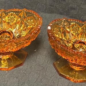 Puede incluir: Dos cuencos de pedestal de vidrio ámbar con un patrón de diamante. Los cuencos están sobre una superficie oscura.