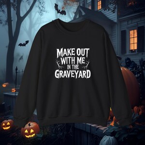 Peut inclure: Sweat-shirt noir avec l'inscription blanche "MAKE OUT WITH ME IN THE GRAVEYARD". Le design a un thème d'Halloween, avec des chauves-souris et des citrouilles en arrière-plan. Parfait pour la saison effrayante.