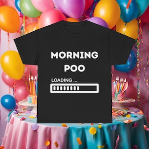Può includere: T-shirt nero con la scritta bianca "MORNING POO", con "LOADING..." e una barra di avanzamento. La maglietta è presentata in un'ambientazione festosa con palloncini colorati e un tavolo decorato.