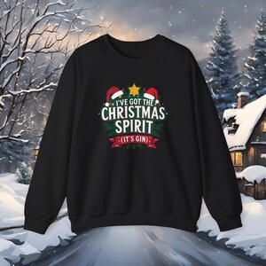 May include: Black crew neck sweatshirt with the text "I'VE GOT THE CHRISTMAS SPIRIT (IT'S GIN)". The design includes Santa hats, a star, and a green wreath. The sweatshirt is perfect for the holiday season.