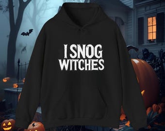May include: Black hooded sweatshirt with the text "I SNOG WITCHES" in white. The sweatshirt has a front pocket and a drawstring hood. The background features a spooky Halloween scene with pumpkins and bats.