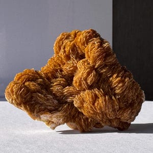 Può includere: Un grande cristallo di selenite marrone, di formazione naturale, con un aspetto unico, a strati e testurizzato. Il cristallo ha una texture delicata, quasi piumosa.