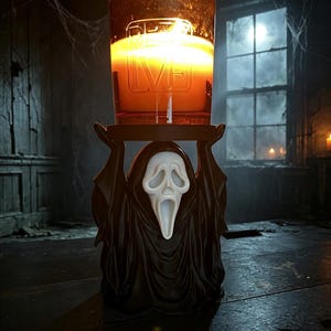 May include: A black candle holder shaped like a hooded figure with a white ghost mask, holding a glass candle jar with a glowing orange flame. The glass jar features the embossed text REVIVE, and the figure has raised arms supporting the candle.