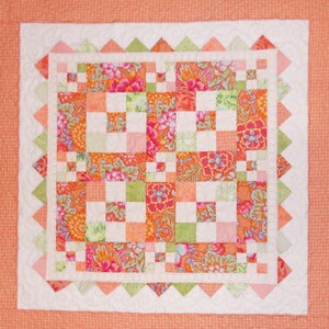 May include: A patchwork quilt with a white background and a variety of floral patterns in shades of pink, orange, and green. The quilt is bordered with a scalloped edge.