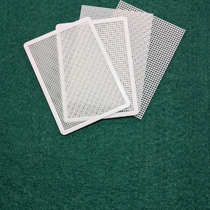 May include: A set of three rectangular white plastic canvas sheets featuring a uniform grid pattern of small square holes. The sheets are layered on top of each other, displaying a consistent mesh structure throughout each piece.