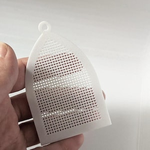 May include: A white, semi-translucent plastic grid sheet shaped like a pointed arch, featuring a uniform square mesh pattern throughout its surface and a small circular loop at the top for hanging or attachment purposes.