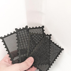 May include: A set of four black plastic grid sheets, each featuring a rectangular shape with scalloped, stamp-like edges. The sheets have a uniform, perforated mesh pattern throughout, designed for crafting or needlepoint projects.