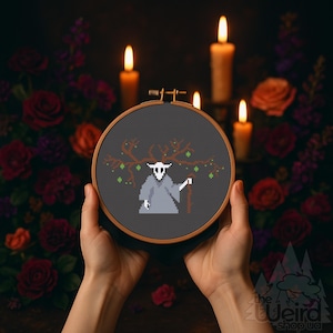 May include: A cross-stitch embroidery in a wooden hoop features a pixelated figure in a grey robe with a skull-like face, holding a staff. The design includes a tree branch with green accents. The background is dark with lit candles and flowers.