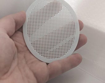 Może przedstawiać: Okrągła tarcza z białej plastikowej siatki z jednolitym wzorem siatki z małymi kwadratowymi perforacjami na całej powierzchni. Tarcza posiada małą zintegrowaną pętelkę na górnej krawędzi, przeznaczoną do zawieszania.