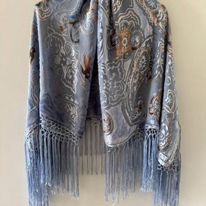 Puede incluir: Un chal azul claro con un patrón de paisley y ribete de flecos.