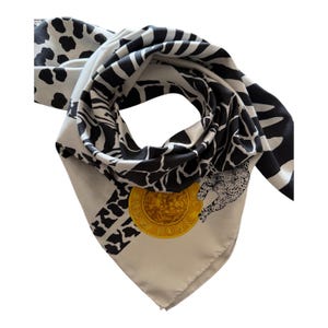 May include: A square scarf featuring a black and white animal print pattern with zebra stripes and leopard spots. A circular gold-coloured emblem is printed on the fabric, displaying the text NEW YORK and an illustration of a leopard.