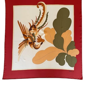 May include: A square silk scarf with a red border and a cream-colored center. The center features a stylized bird and foliage in shades of brown, orange, and green. The scarf has a vintage aesthetic.