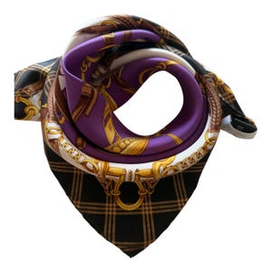 May include: A square scarf featuring a vibrant purple center surrounded by a white border with gold-toned chain and equestrian buckle motifs. The outer edges display a black and tan plaid pattern, creating a contrast between the geometric lines and the ornate, curved metallic elements printed on the fabric.