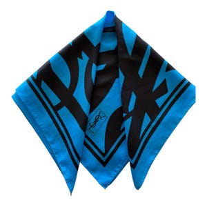 May include: Square silk scarf in black and turquoise blue. The scarf features a bold, abstract design with the brand's logo in the corner. The scarf has a turquoise blue border.