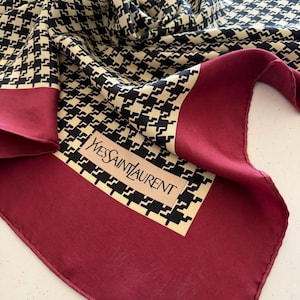 May include: A silk scarf with a houndstooth pattern in black and cream, framed by a deep burgundy border. The scarf features the "Yves Saint Laurent" logo in the corner.