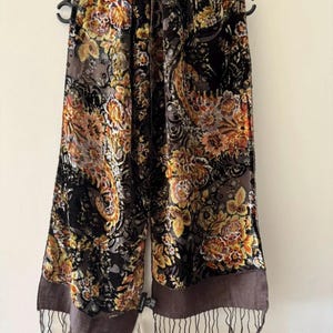 Könnte beinhalten: Ein brauner und schwarzer Samt-Schal mit einem floralen Muster in Orange-, Gelb- und Rottönen. Der Schal hat unten einen Fransenbesatz und einen braunen Rand.