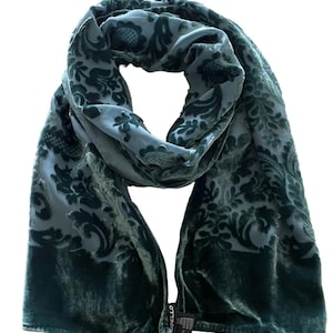 May include: A teal-colored scarf with a floral damask pattern. The scarf is made of a soft, velvety material and has a darker teal border. The scarf is draped and folded, showcasing the intricate design and texture.
