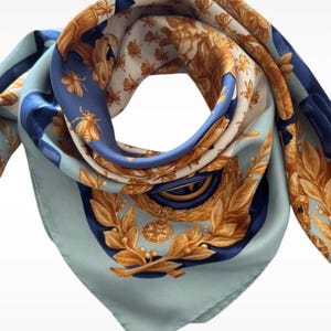 Peut inclure: Un foulard carré bleu clair orné d'un motif répétitif d'abeilles dorées et de couronnes de laurier complexes dans des tons dorés et bleu foncé. Le design présente un emblème circulaire central entouré de feuillage, avec une texture lisse et pliée.