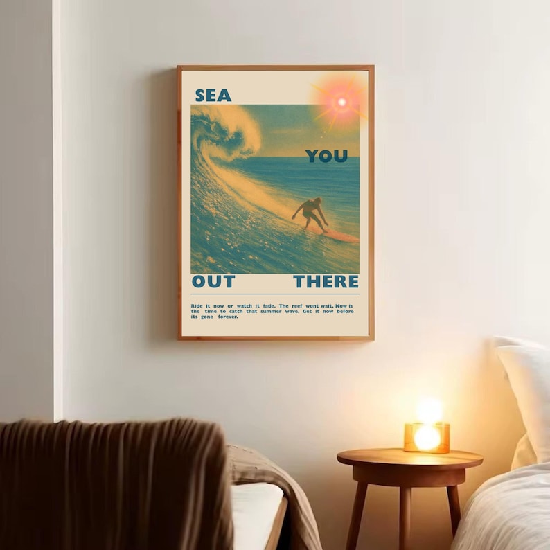 May include: Framed poster with a vintage aesthetic. The artwork features a surfer riding a wave, with the words "SEA YOU OUT THERE" in bold letters. The poster has a warm color palette with a sun illustration.