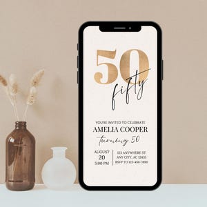Puede incluir: Un tel&eacute;fono inteligente muestra una invitaci&oacute;n digital para el 50 cumplea&ntilde;os de Amelia Cooper. El dise&ntilde;o presenta n&uacute;meros y escritura dorados, con detalles del evento, como la fecha, la hora y el lugar. Un jarr&oacute;n marr&oacute;n con flores secas y un jarr&oacute;n blanco est&aacute;n en el fondo.